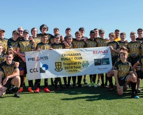Group photo of Crusaders Rugby Club players in Oakville posing on a grassy rugby field while holding a banner.
