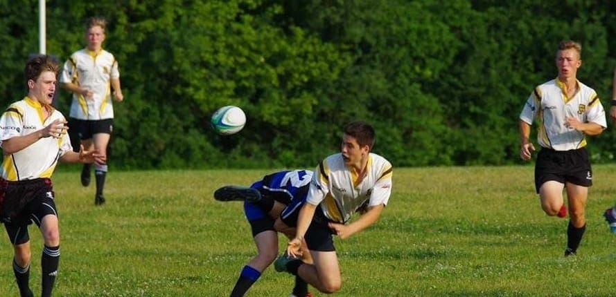 Aurora2 Rugby players in cream and black jerseys chase the ball on a grassy field at Crusaders Rugby Club in Oakville.