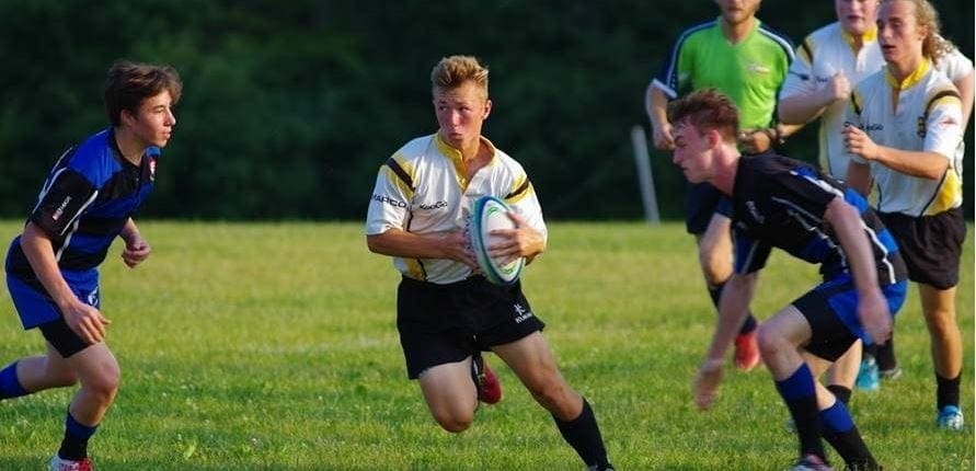 Aurora3 Crusaders Rugby Club players from Oakville run with the ball during a rugby match on a grassy field.