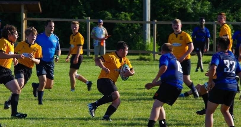 MT1 Crusaders Rugby Club players in yellow and blue jerseys compete on a sunny grassy field.