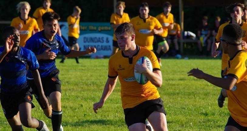 MT7 Crusaders Rugby Club players in yellow and blue jerseys play rugby on a grassy field in Oakville.