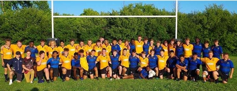 MT9 Group photo of the Crusaders Rugby Club in Oakville on a rugby field with goalposts, players wearing yellow and blue jerseys.