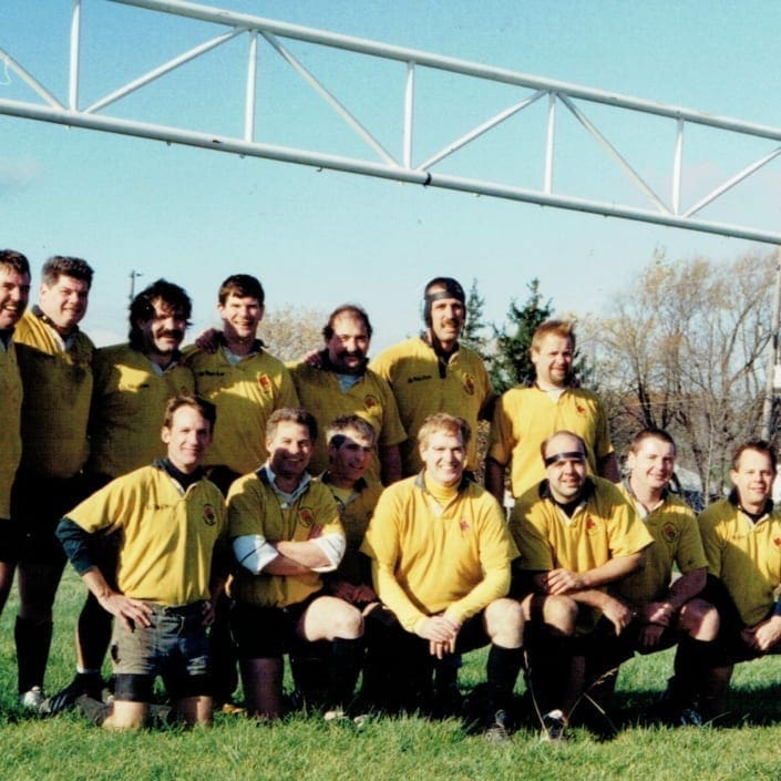 Group photo of Crusaders Rugby Club players in yellow and brown jerseys on a rugby field in Oakville.