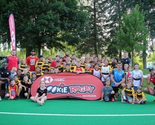 Group photo of Crusaders Rugby Club players and coaches in Oakville posing on a green field with a red Rookie Rugby banner.