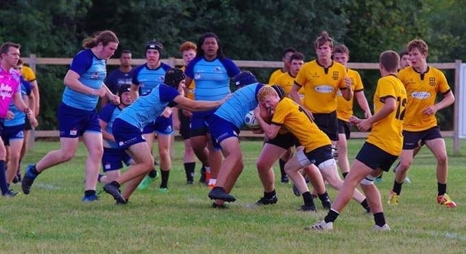 Crusaders Rugby Club Oakville players in blue and yellow jerseys compete in a rugby match on a grassy field.