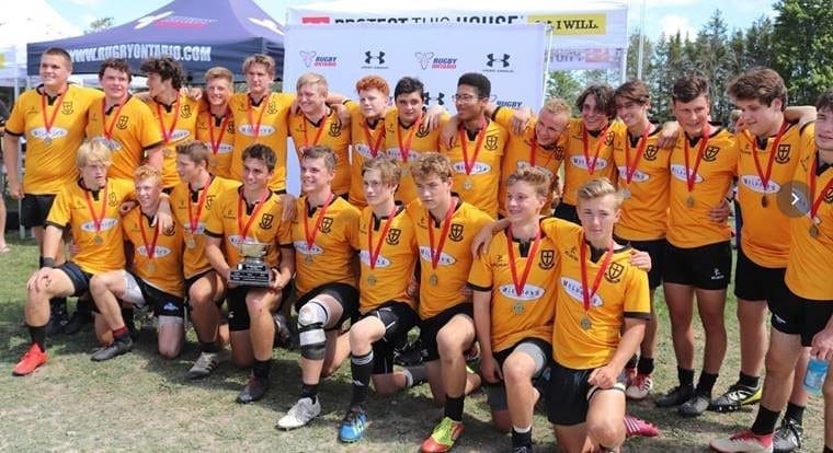 Group of Crusaders Rugby Club players in orange jerseys pose for a team photo with medals on a rugby field in Oakville.