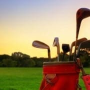 Red golf bag with clubs on a grassy field at sunset.
