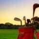 Red golf bag with clubs on a grassy field at sunset.
