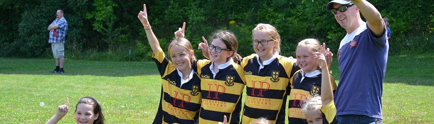 A youth rugby team in black-and-yellow striped jerseys posing with a coach on a grassy field.