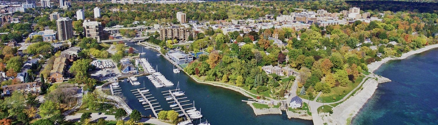 Aerial view of a waterfront Oakville neighborhood with a marina, boats, and tree-lined streets along the shoreline. Aerial view of a waterfront Oakville neighborhood with a marina, boats, and tree-lined streets along the shoreline.