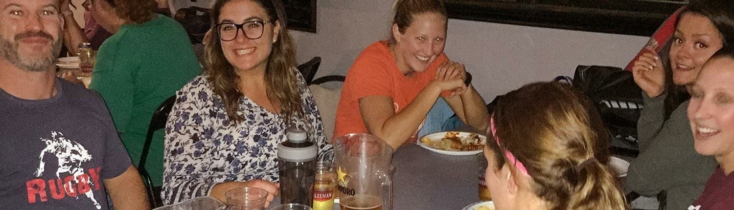 Crusaders Rugby Club members from Oakville sit around a table in a casual restaurant, chatting and enjoying drinks.