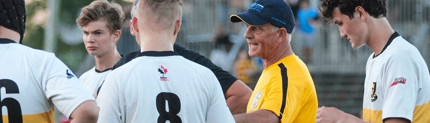 Crusaders Rugby Club players in white numbered jerseys stand with a coach in a yellow shirt on the rugby field.