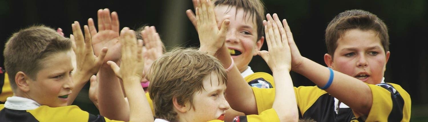 Crusaders Rugby Club players in yellow and black jerseys celebrating with a group high-five.