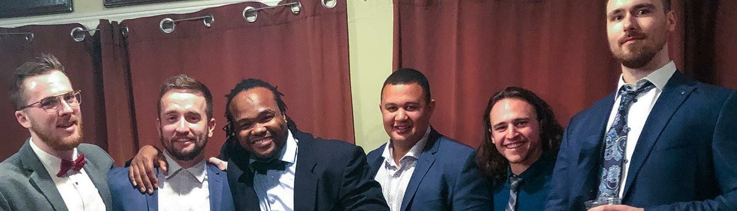 Six men in suits pose together indoors at Crusaders Rugby Club in Oakville.