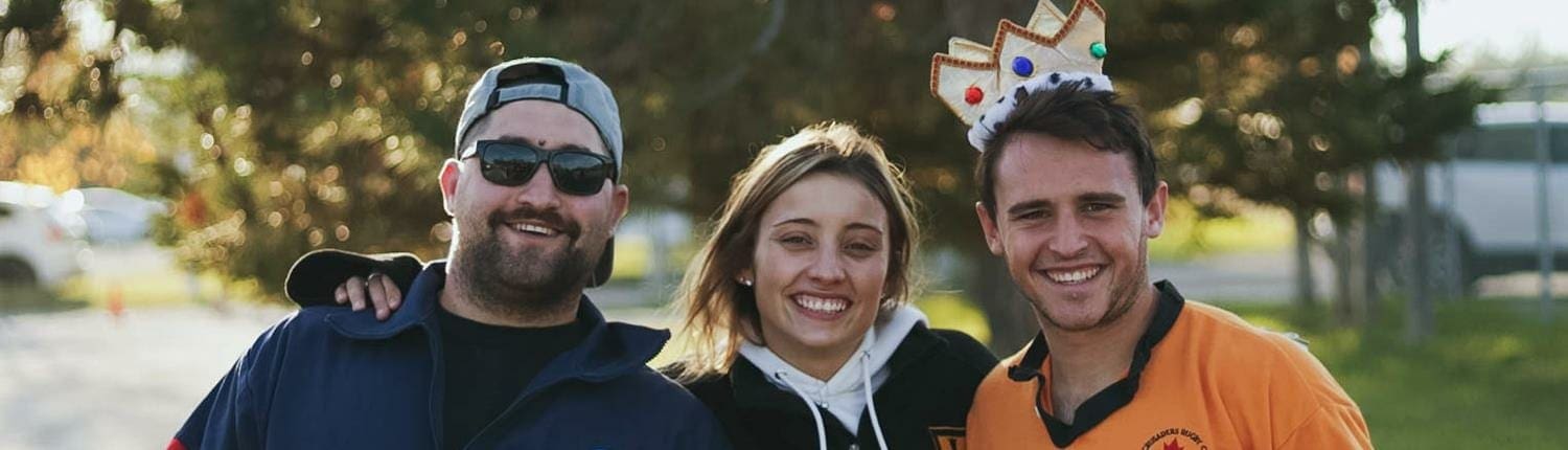 Three people from the Crusaders Rugby Club in Oakville pose outdoors and smile.