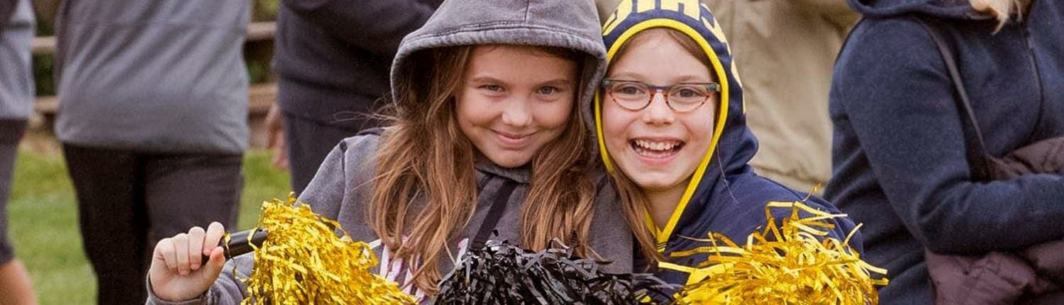 Two smiling girls cheer with yellow pom-poms at the Crusaders Rugby Club in Oakville.