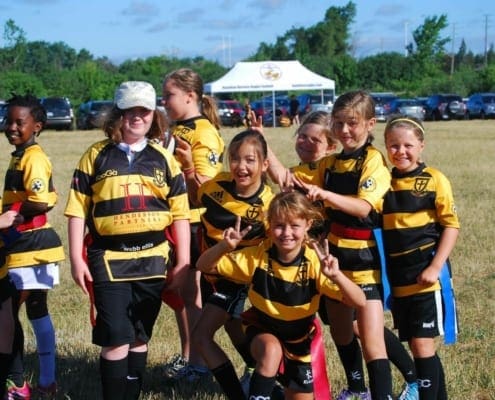 Young Crusaders Rugby Club players from Oakville pose together on a sunny field, wearing yellow and black striped jerseys.