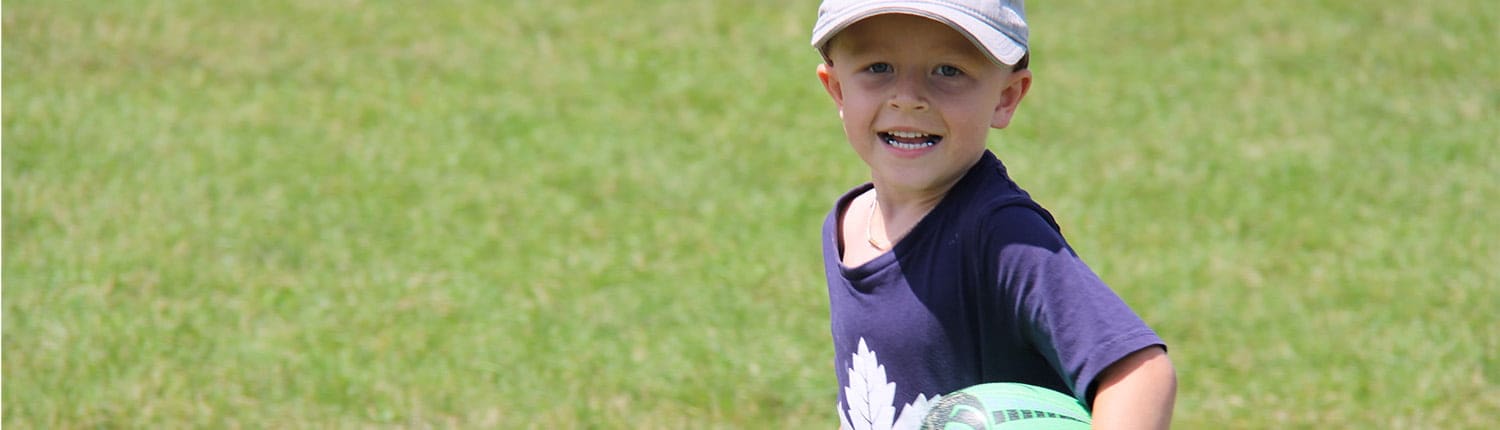 A young Crusaders Rugby Club player in Oakville, wearing a dark shirt and white cap, holding a rugby ball on a grassy field. A young Crusaders Rugby Club player in Oakville, wearing a dark shirt and white cap, holding a rugby ball on a grassy field.