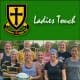 Group of women rugby players posing outdoors in front of a Crusaders Rugby Club crest and a green banner reading “Ladies Touch.”