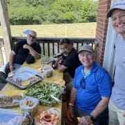 Crusaders Rugby Club members in Oakville sit at an outdoor table with assorted food trays, smiling.