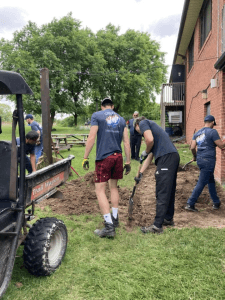 Crusaders Rugby Club members in Oakville dig with shovels beside a brick building.