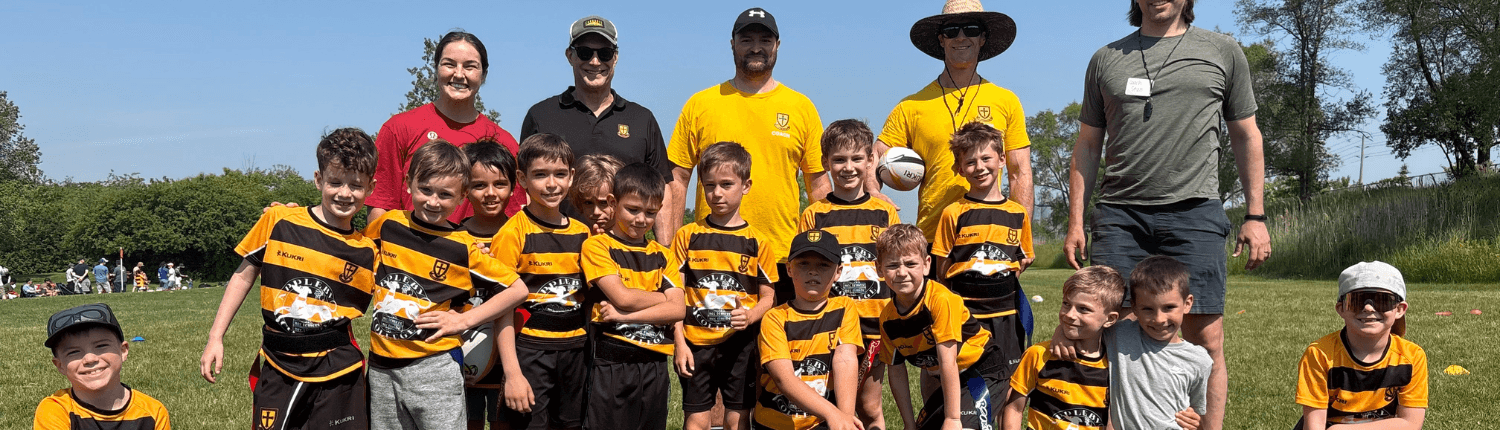 Crusaders youth rugby team and coaches in black-and-yellow striped jerseys on sunny field.