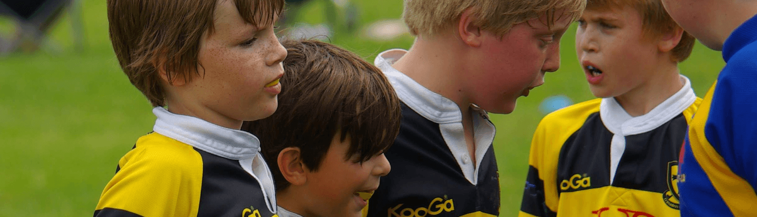 Youth rugby team in yellow and navy jerseys standing on a grassy Oakville field.