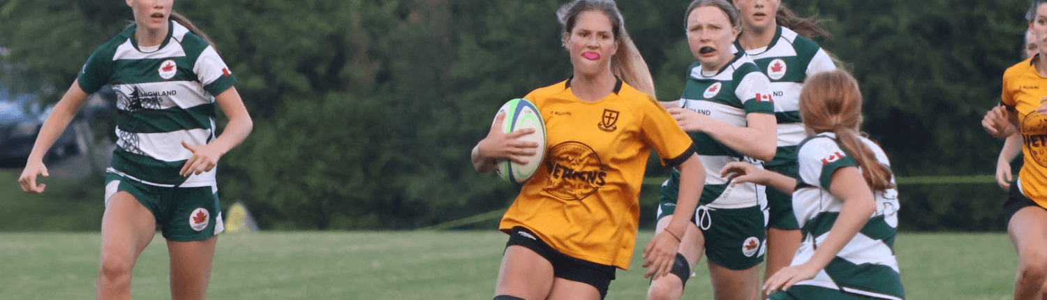 2025 Junior Girls Crusaders Rugby Club Oakville players in green and yellow uniforms compete on a grassy field, with a central player in yellow holding a rugby ball.