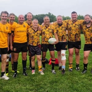 2025 Fab 4s Group of Crusaders Rugby Club players in Oakville posing on a grassy field in yellow and patterned jerseys, with a rugby ball in the center.