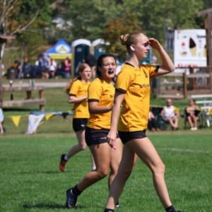 2024-U16G Girls' rugby players in yellow jerseys walk across a grassy field at Crusaders Rugby Club in Oakville.