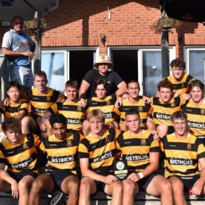 U18B-2023 Crusaders Rugby Club players pose for a team photo on the steps of a brick building in Oakville, wearing black and yellow striped jerseys.