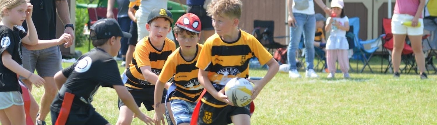 Kids playing flag rugby on a sunny grass field during youth sports training.