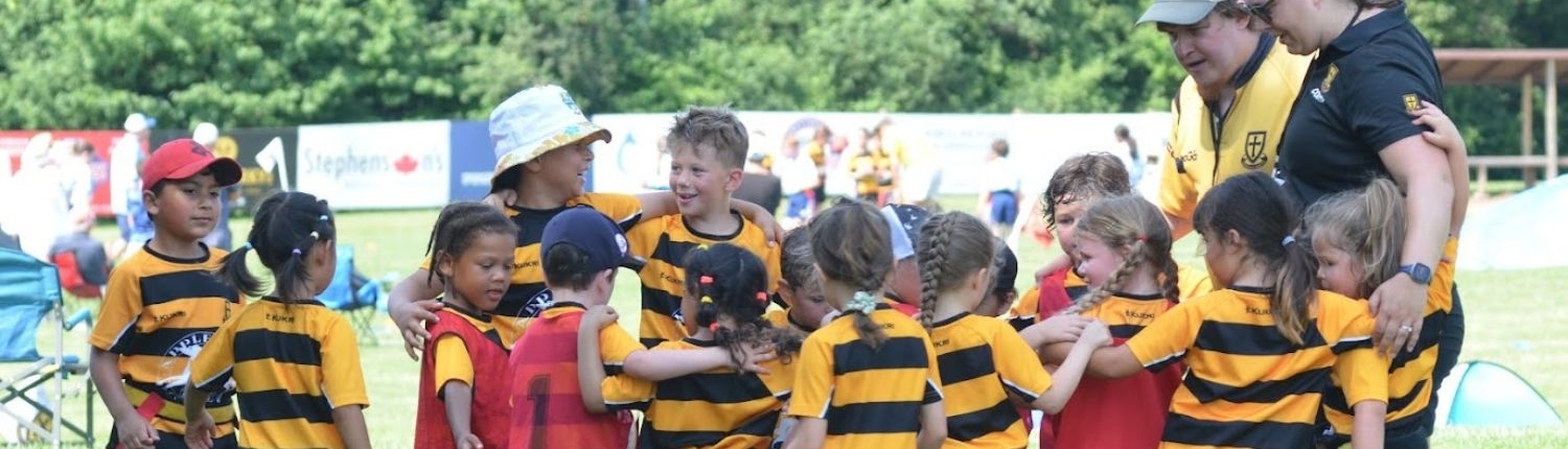 Kids Rugby Team Huddle on Sunny Field Youth rugby team in yellow and black jerseys huddling with coaches on a sunny grass field.