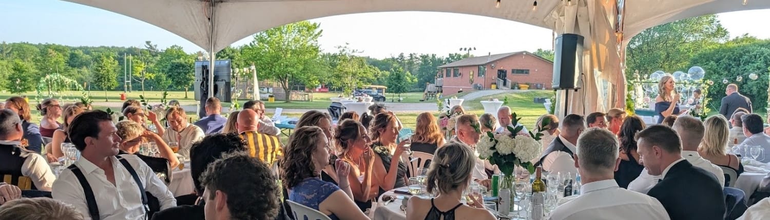 Outdoor gathering of Crusaders Rugby Club members and guests seated at long tables under a canopy in Oakville.