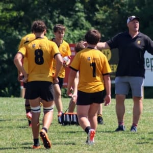 U16B-2025 with Attie Crusaders Rugby Club players in yellow jerseys on a grassy field with a coach giving instructions.